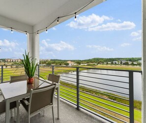 A balcony with a table and chairs, overlooking a body of water and greenery.