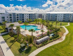 A modern hotel with a central pool surrounded by palm trees and outdoor seating.