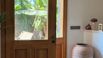 Una puerta de madera con un panel de vidrio, una gran maceta de barro y un estante con adornos.