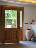 A wooden door with a glass panel, a large clay pot, and a small shelf with decorative items.
