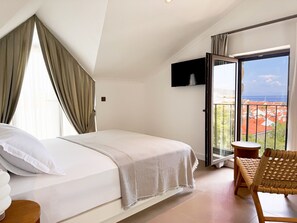 Un dormitorio con cama, una silla, televisor y balcón con vistas.