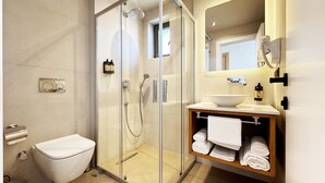 Un baño moderno con ducha envuelta en vidrio, inodoro blanco y tocador con lavamanos y toallero.