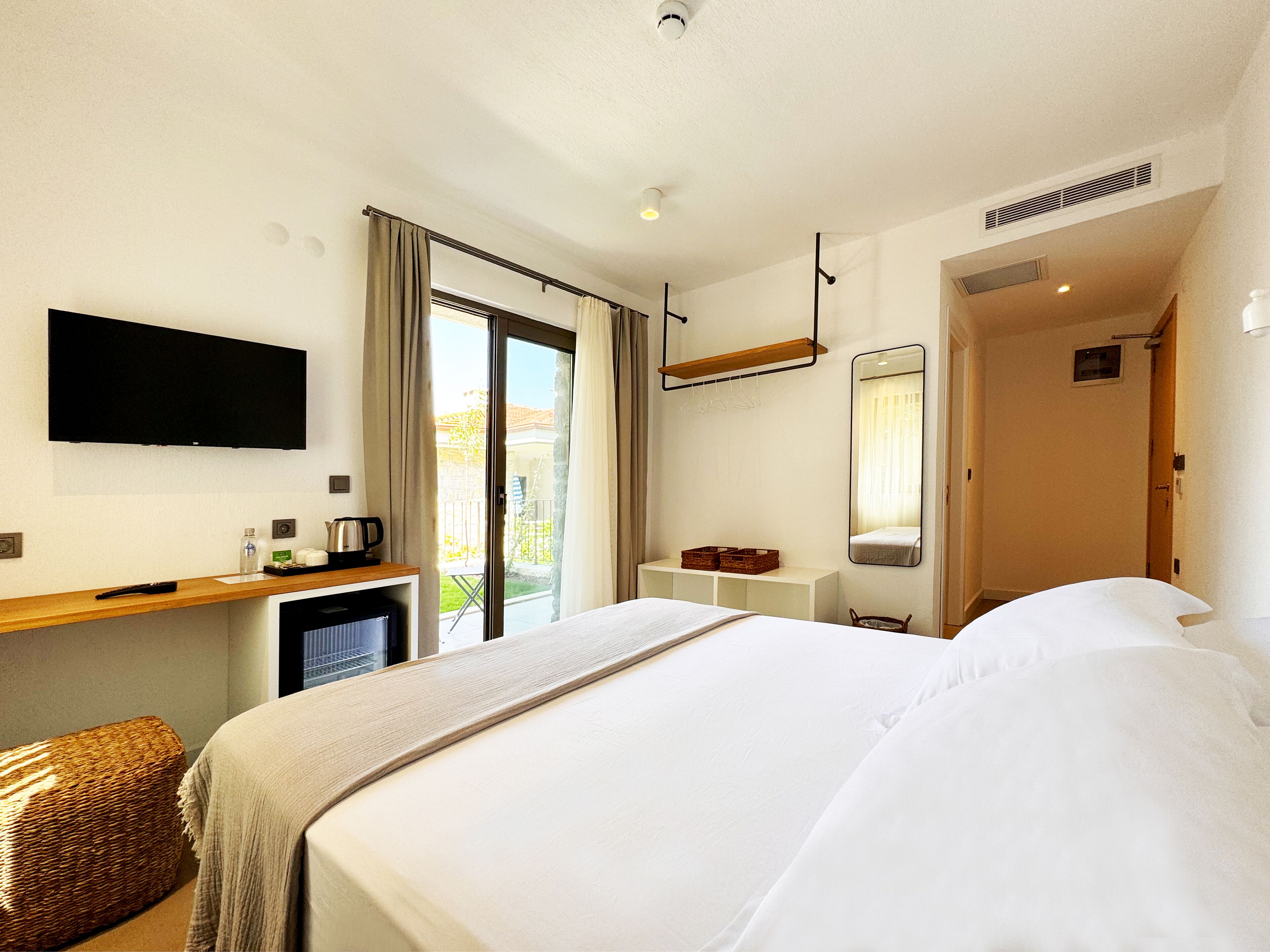 Ein Hotelzimmer mit einem Bett, einem Flachbildfernseher, einem Schreibtisch mit Kaffeemaschine, einem kleinen Kühlschrank und einer Schiebetür zum Balkon.