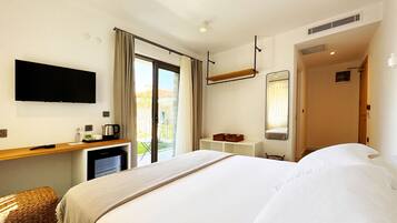 Ein Hotelzimmer mit einem Bett, einem Flachbildfernseher, einem Schreibtisch mit Kaffeemaschine, einem kleinen Kühlschrank und einer Schiebetür zum Balkon.