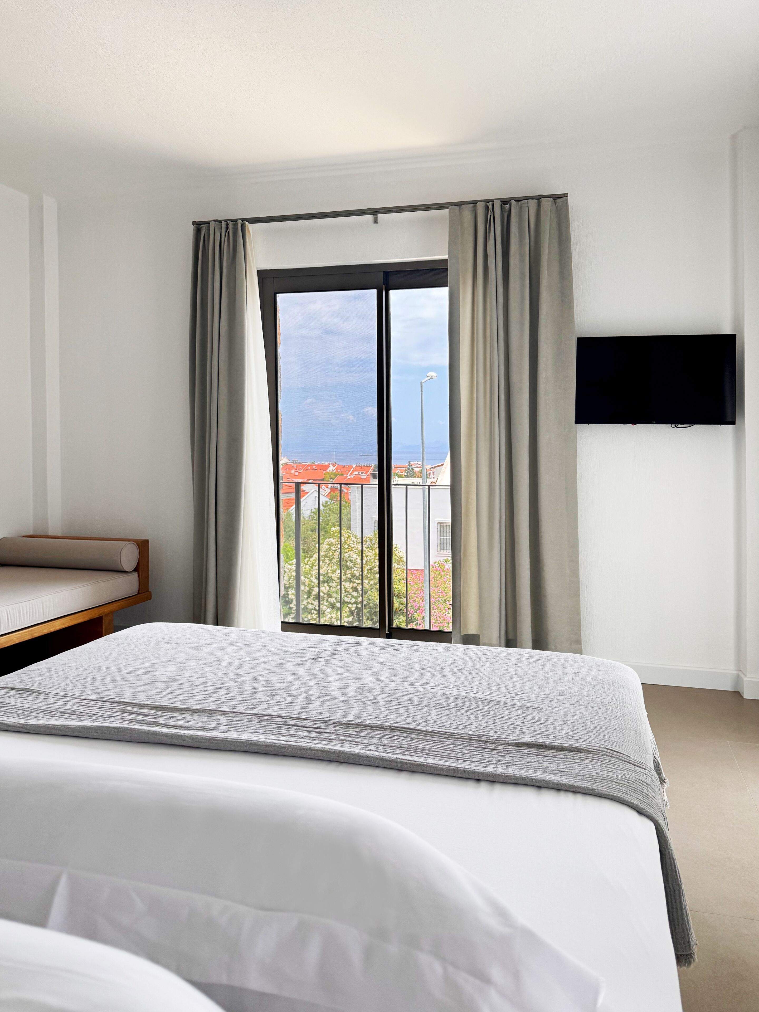Habitación de hotel con cama, sofá, televisor montado en la pared y balcón con vistas al mar.