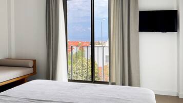 Habitación de hotel con cama, sofá, televisor montado en la pared y balcón con vistas al mar.