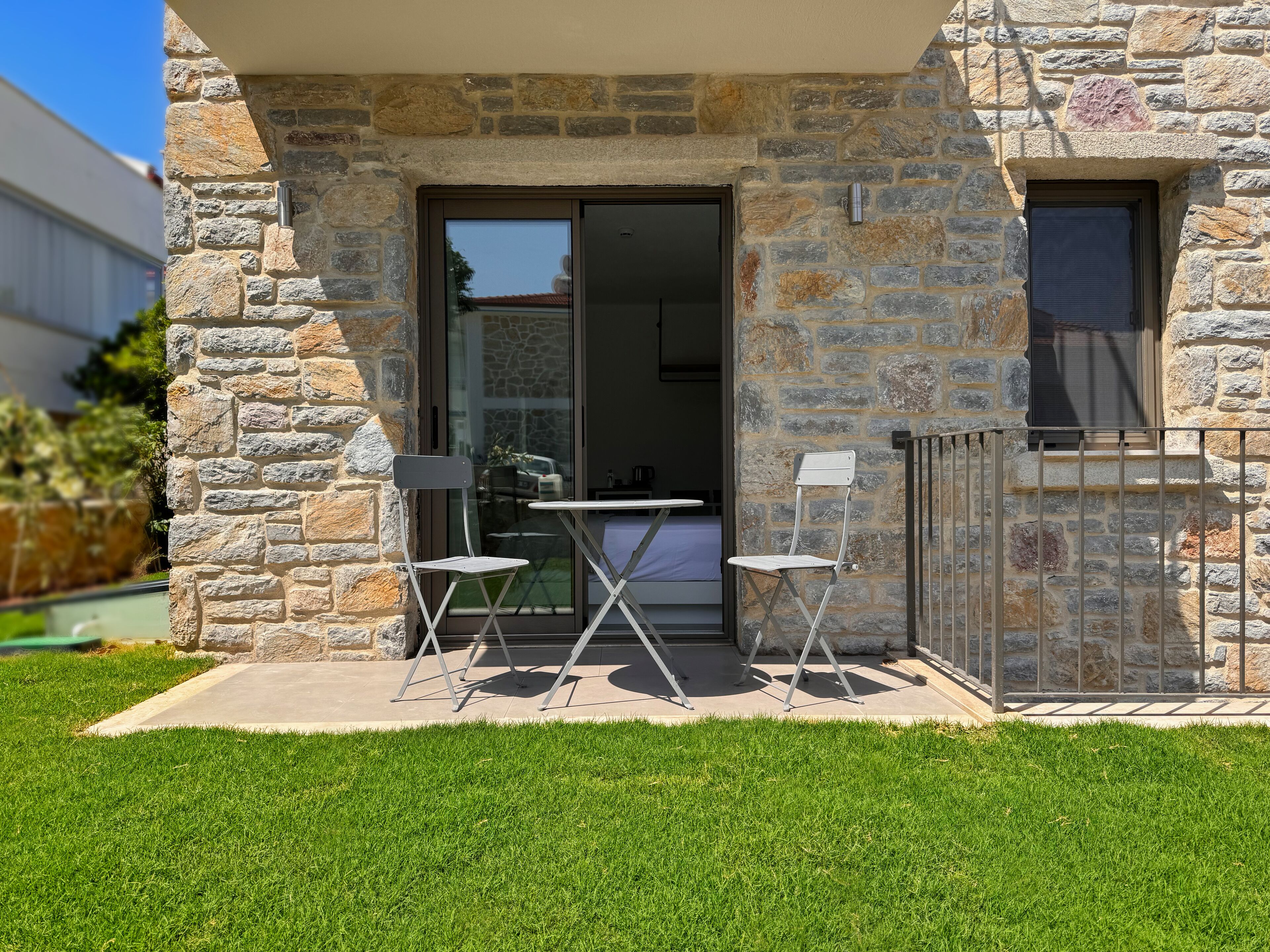 A stone building with a glass door, two white folding chairs, and a small table.