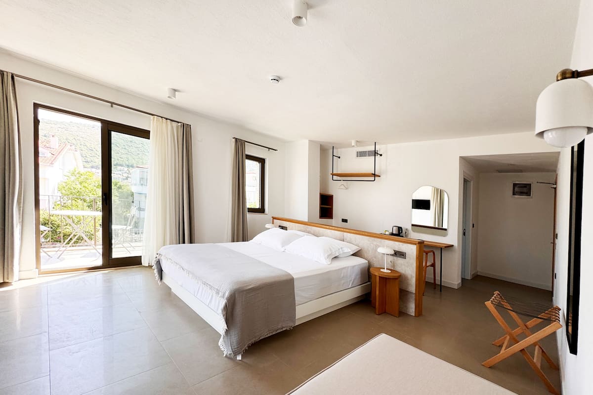 A spacious bedroom with a large bed, a desk, and a chair. There is a sliding glass door leading to a balcony.