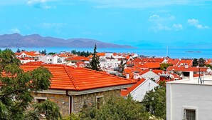 Un pueblo costero con edificios de techo rojo, cielo azul despejado y montañas al fondo.