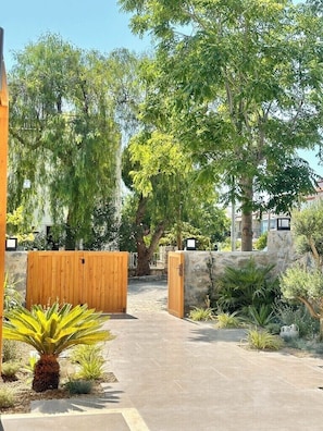 A gated entrance with a pathway leading to a building, surrounded by trees and plants. - VİLLA KANTARLI (Datça)