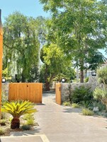 A gated entrance with a pathway leading to a building, surrounded by trees and plants.
