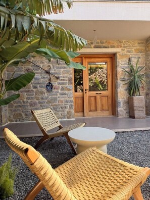 Un espacio al aire libre con paredes de piedra, una puerta de madera, muebles de mimbre y plantas en macetas.