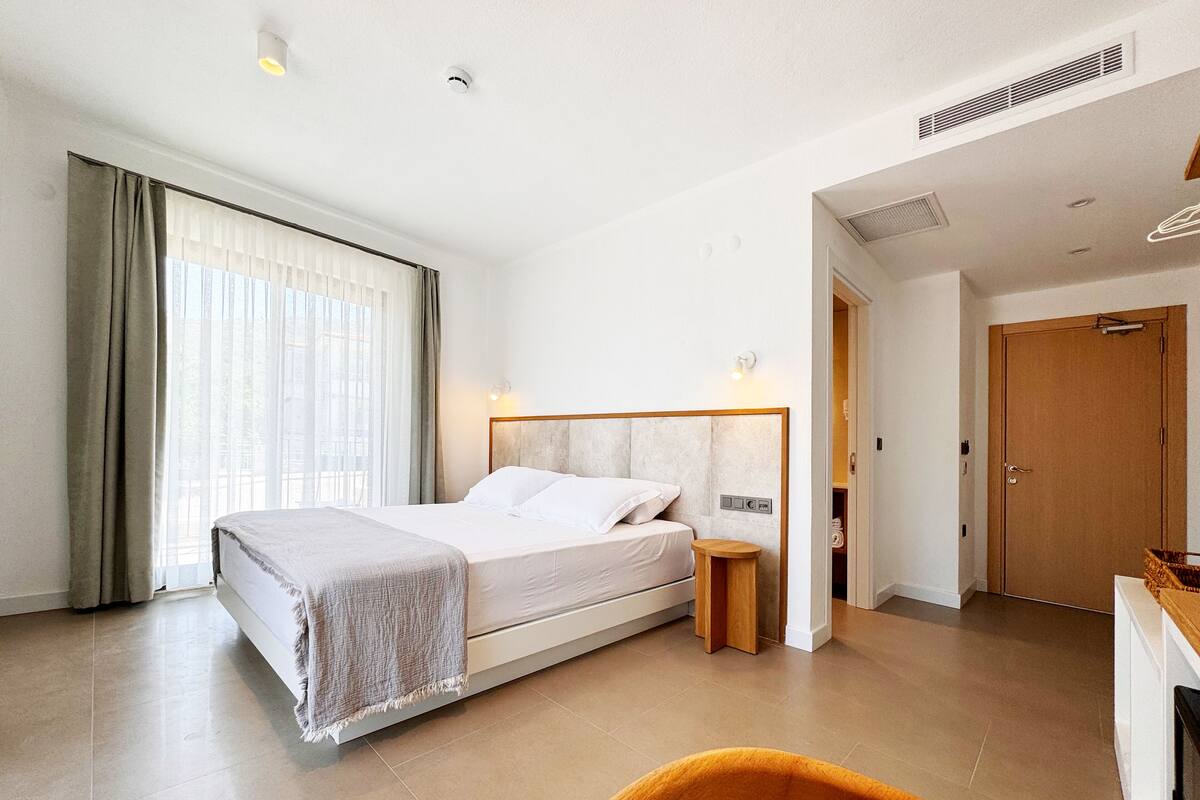 A hotel room with a bed, bedside table, and a view of the outside through the window.