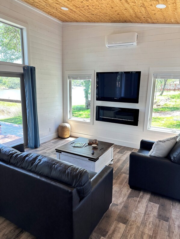 Una sala de estar moderna con televisor de pantalla plana, chimenea y ventanas amplias con vistas a un jardín.