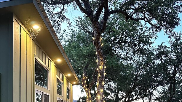 A modern house with a wooden deck, large windows, and a tree decorated with lights.