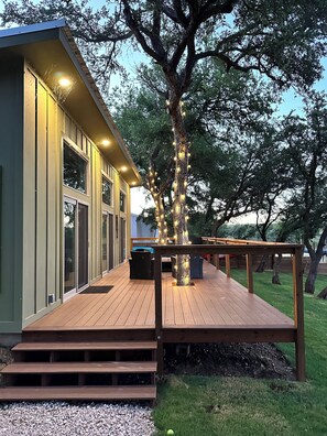Una casa moderna con terraza de madera, ventanas amplias y un árbol adornado con luces.