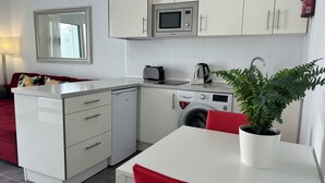 A compact kitchen with a microwave, toaster, and washing machine. There is a dining table with red chairs and a potted plant. - Cozy 1 bedroom apartment on a popular complex (Puerto del Carmen)