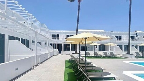 A poolside area with lounge chairs and umbrellas, a clear sky, and palm trees. - Cozy 1 bedroom apartment on a popular complex (Puerto del Carmen)