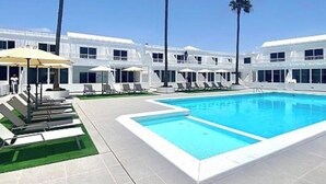 A modern hotel with a large rectangular pool, sun loungers, and palm trees. - Cozy 1 bedroom apartment on a popular complex (Puerto del Carmen)