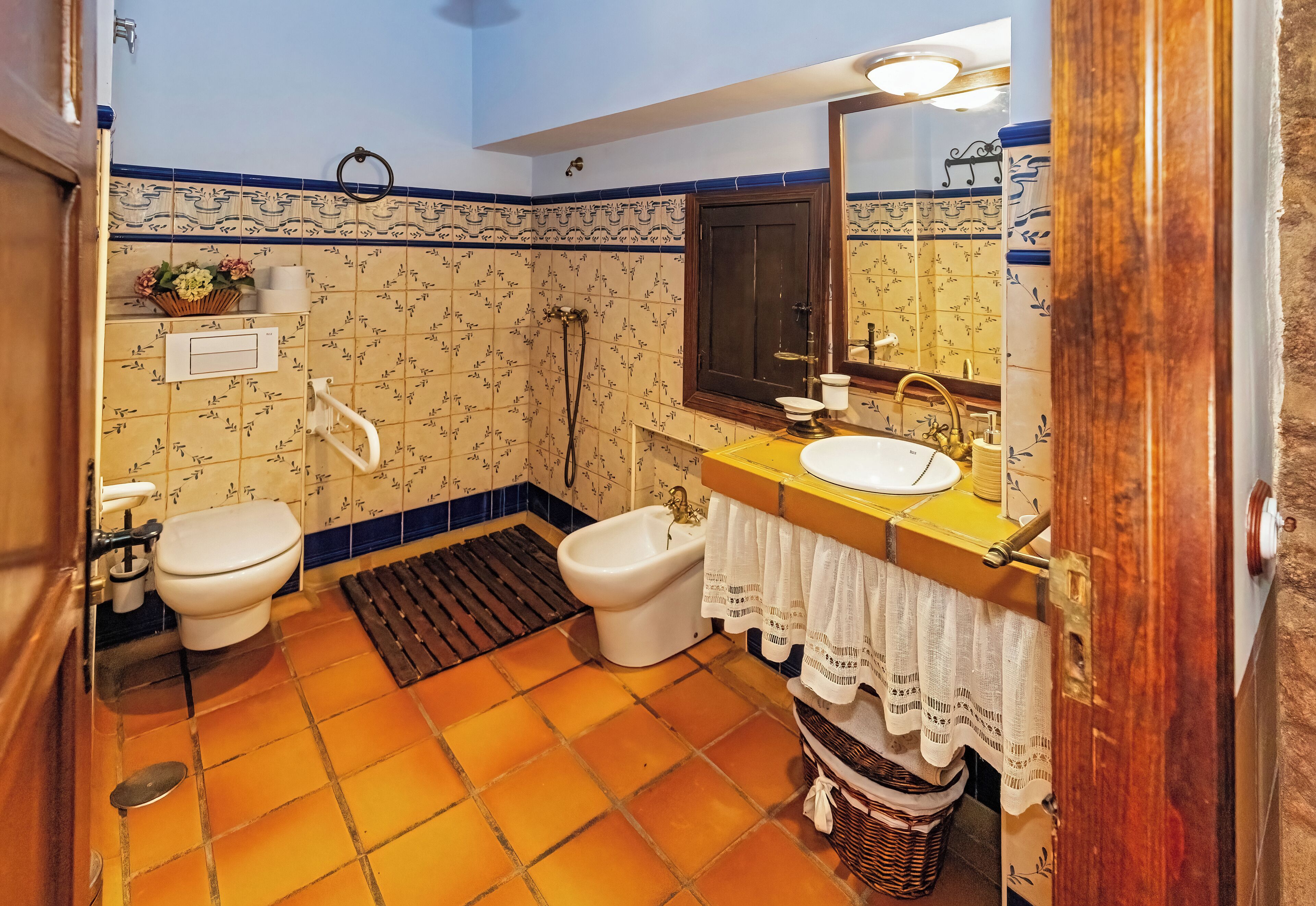 A bathroom with a toilet, bidet, and sink, tiled floor, and a mirror above the sink.