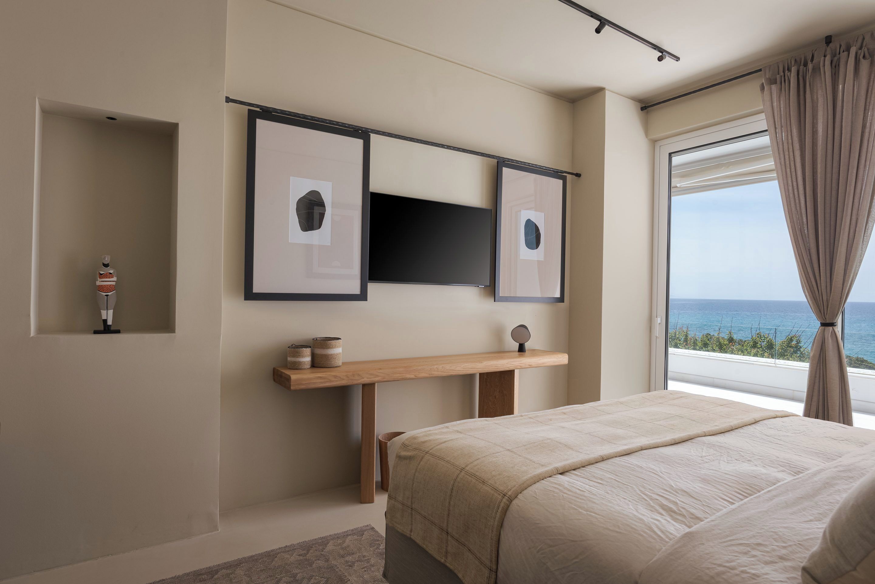 Une chambre à coucher avec un lit, un téléviseur fixé au mur, une table de chevet et une fenêtre donnant sur la mer.