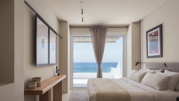 Una camera da letto con un letto grande, un comodino in legno, vista mare dalla finestra e un quadro appeso al muro.