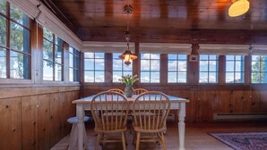 A wooden dining room with a table and chairs, large windows, and a hanging light fixture.