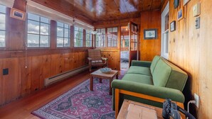 A cozy room with wooden walls, a green sofa, a wooden table, and a patterned rug.