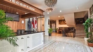 A reception area with a wooden reception desk, a chandelier, and a staircase leading to the upper floor. - Hotel Gino Wellness Rabath (Akhaltsikhe)