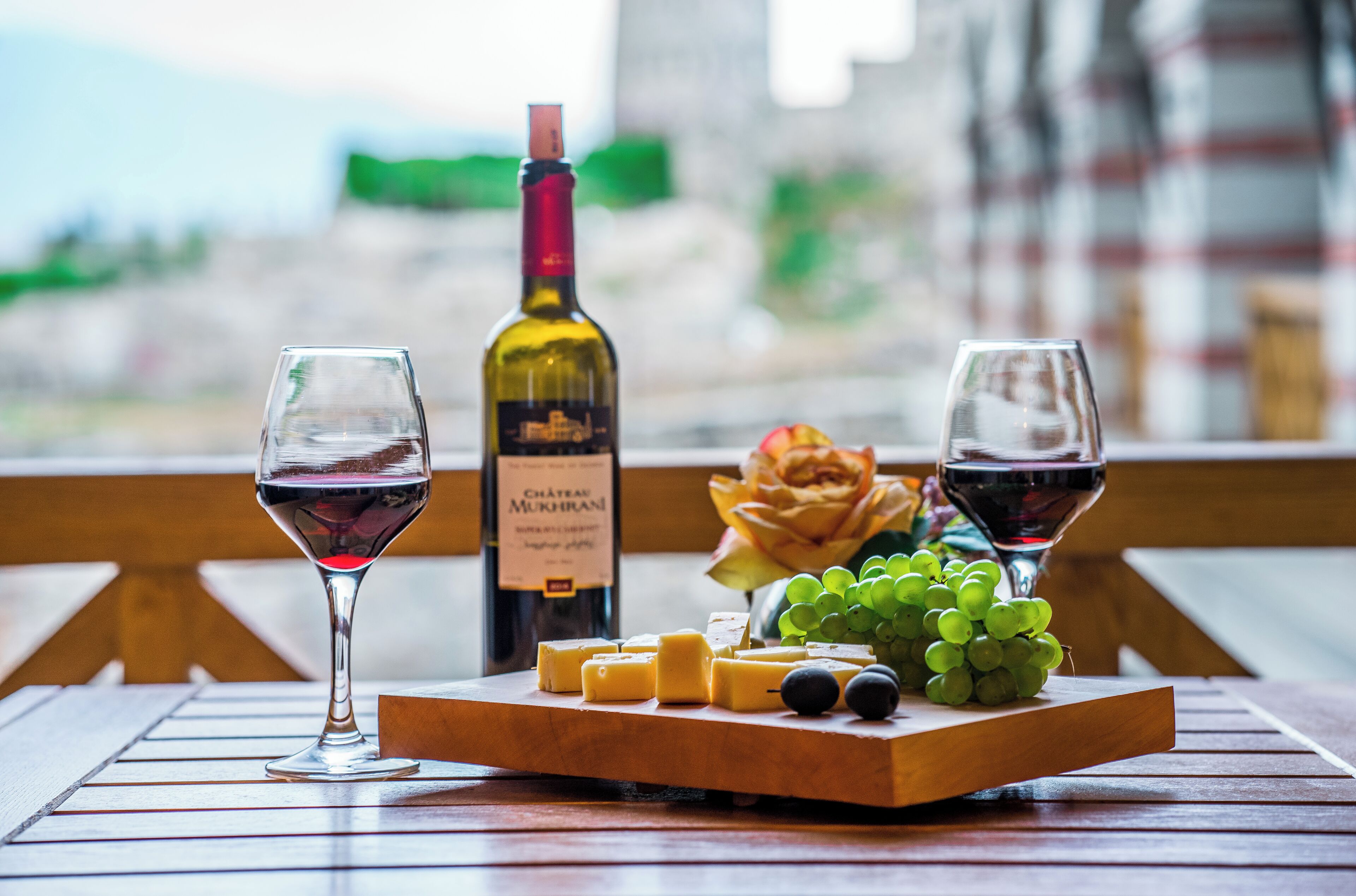 A table with two wine glasses, a bottle of wine, cheese, grapes, and a flower.