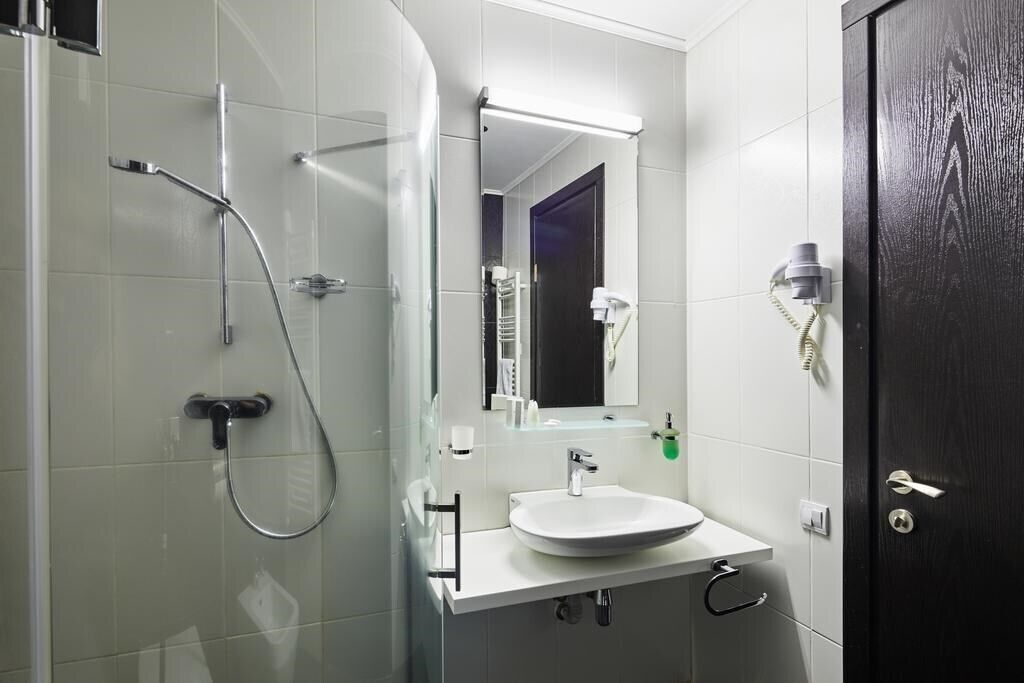 A modern bathroom with a glass shower enclosure, a white sink, and a dark wooden door.