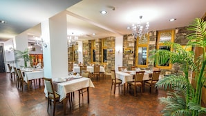 A restaurant with multiple tables and chairs, stone walls, and a chandelier. - Hotel Gino Wellness Rabath (Akhaltsikhe)