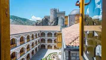 A courtyard with a fountain, a castle in the background, and a building with a tiled roof.