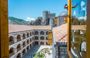 A courtyard with a fountain, a castle in the background, and a building with a tiled roof.