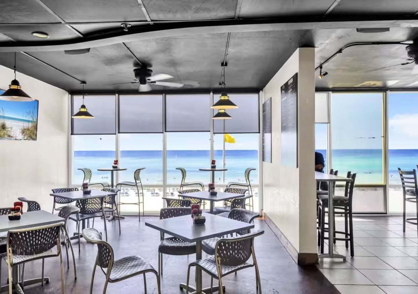 A restaurant with tables and chairs, large windows, and a view of the beach.