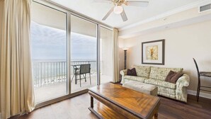 Ein großzügiges Wohnzimmer mit einem großen Schiebeglastür, die auf einen Balkon führt, einem Holztisch, einem gemusterten Sofa und einem gerahmten Bild an der Wand.