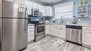 A modern kitchen with white cabinets, stainless steel appliances, a microwave, oven, dishwasher, and a window with blinds.