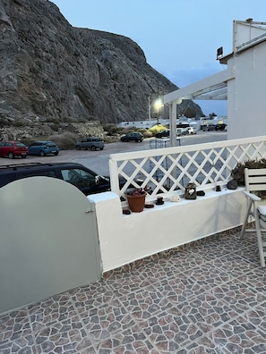 A terrace with a stone floor, white railing, and a potted plant. - Sagma Beach Apartments next to the beach (Santorini)