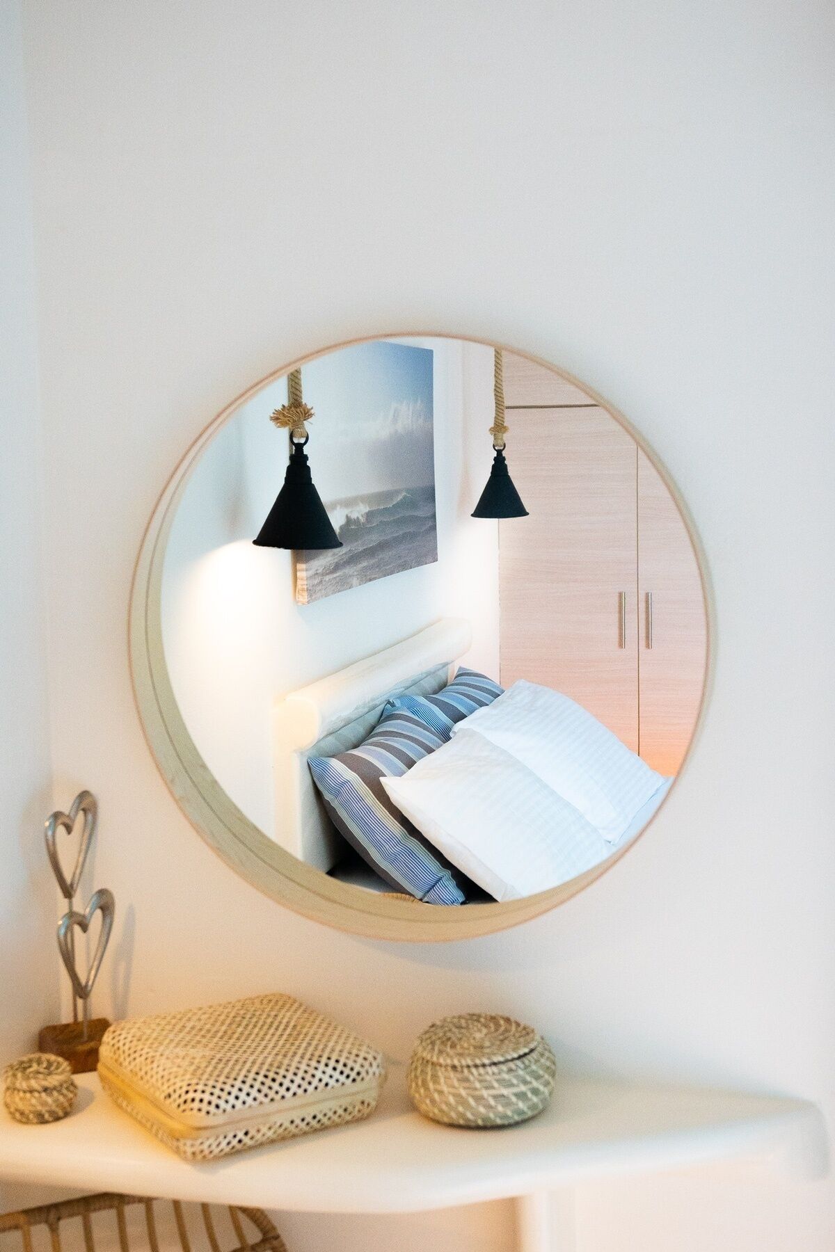 Ein runder Spiegel, der ein Schlafzimmer mit Bett, Kissen, einem Nachttisch und einem Holzschrank reflektiert.
