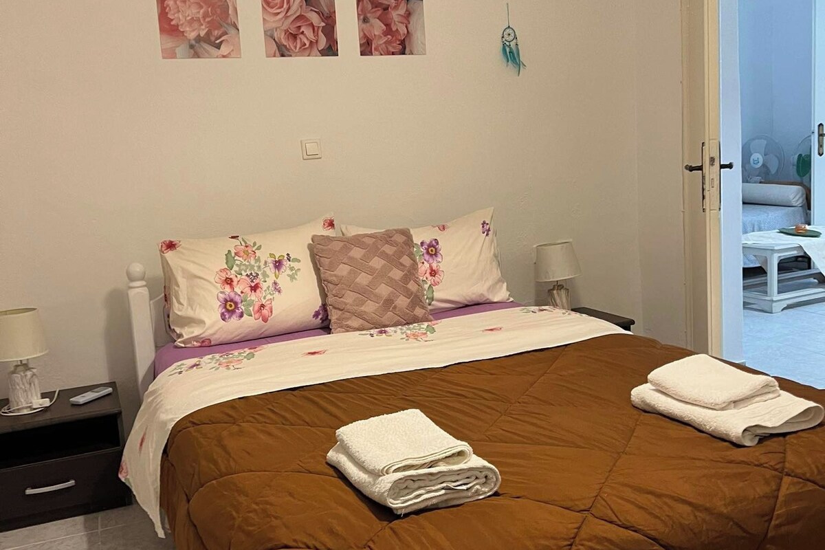 A bedroom with a brown quilted bedspread, floral pillows, and a nightstand with a lamp.