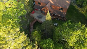 A log cabin with a deck, a fire pit, and a covered outdoor seating area surrounded by dense forest.