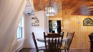 Een eetruimte met een houten tafel en stoelen, een hanglamp en uitzicht op de natuur door een raam.