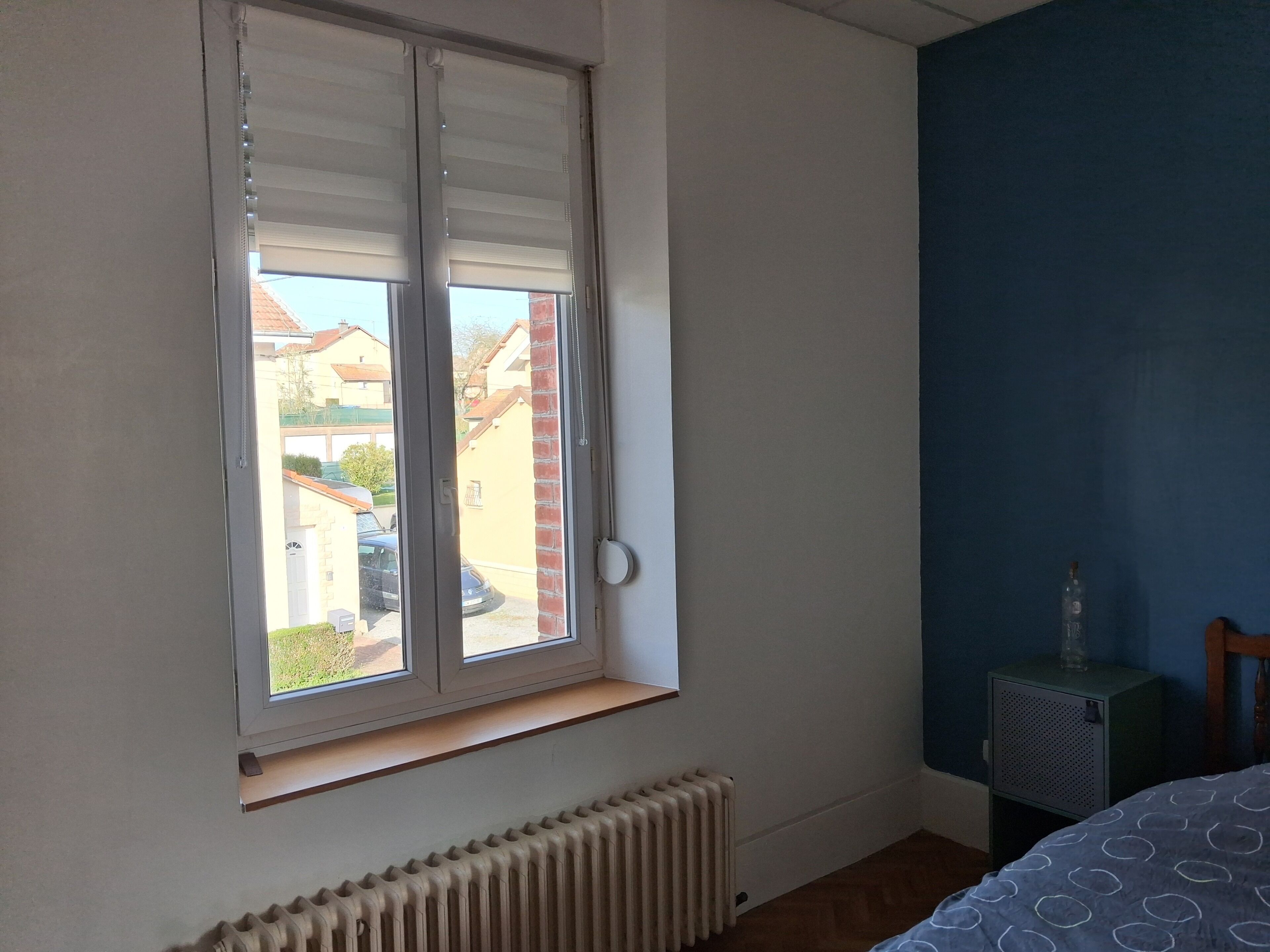 A room with a window, radiator, and a small bedside table.