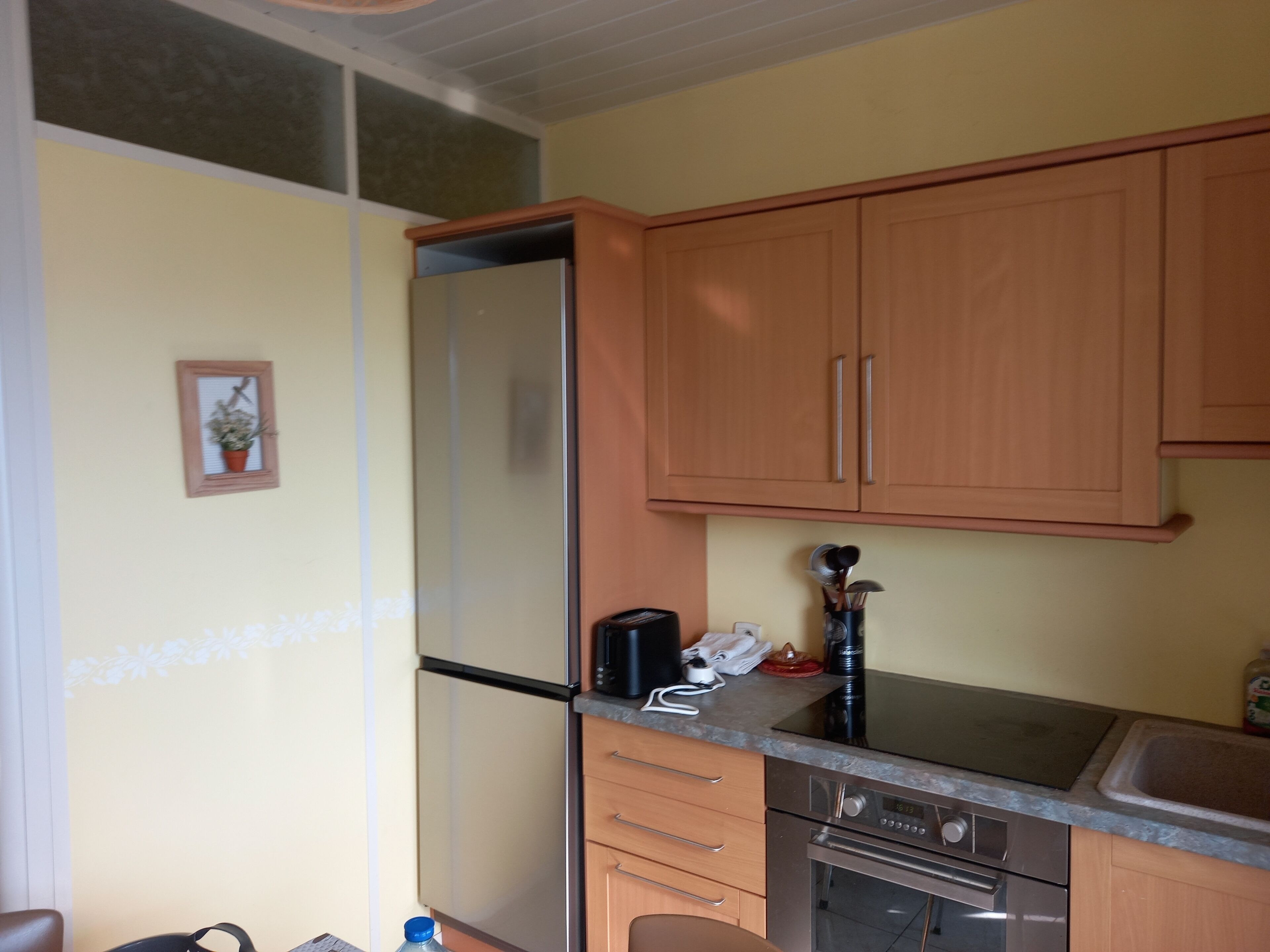 Una cocina compacta con armarios de madera, un refrigerador de acero inoxidable, un horno empotrado y una encimera con cafetera y utensilios.