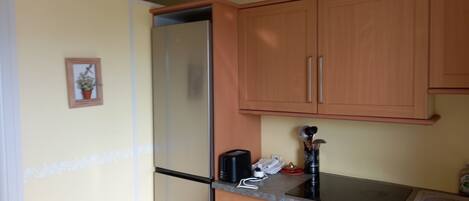 Una cocina compacta con armarios de madera, un refrigerador de acero inoxidable, un horno empotrado y una encimera con cafetera y utensilios.