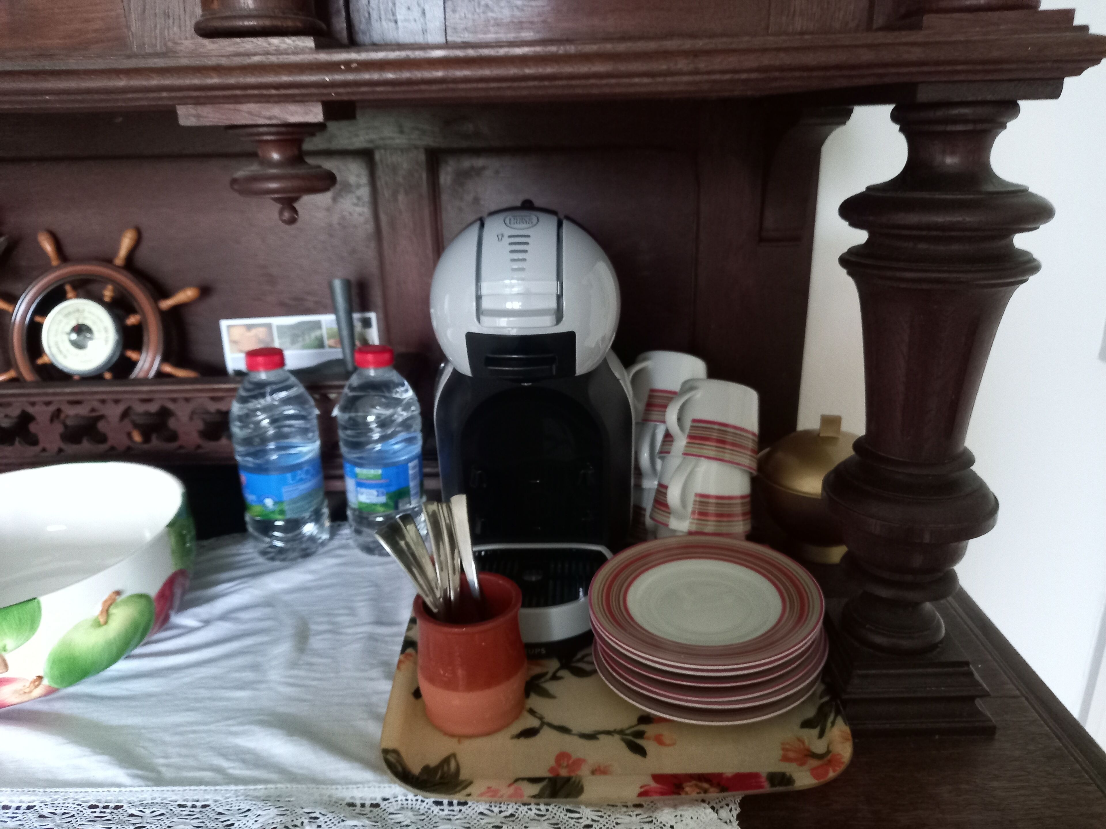 A kitchen counter with a coffee maker, water bottles, a red mug, and stacked plates.