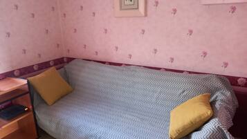 A small, single-bed room with a chevron-patterned bedspread, a wooden nightstand, and a framed picture on the wall.