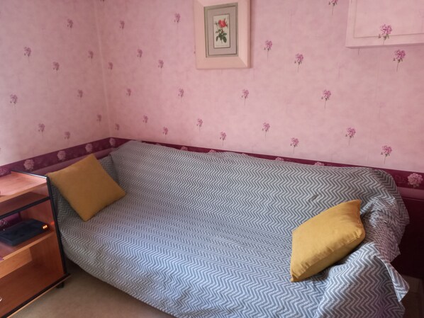 A small, single-bed room with a chevron-patterned bedspread, a wooden nightstand, and a framed picture on the wall.
