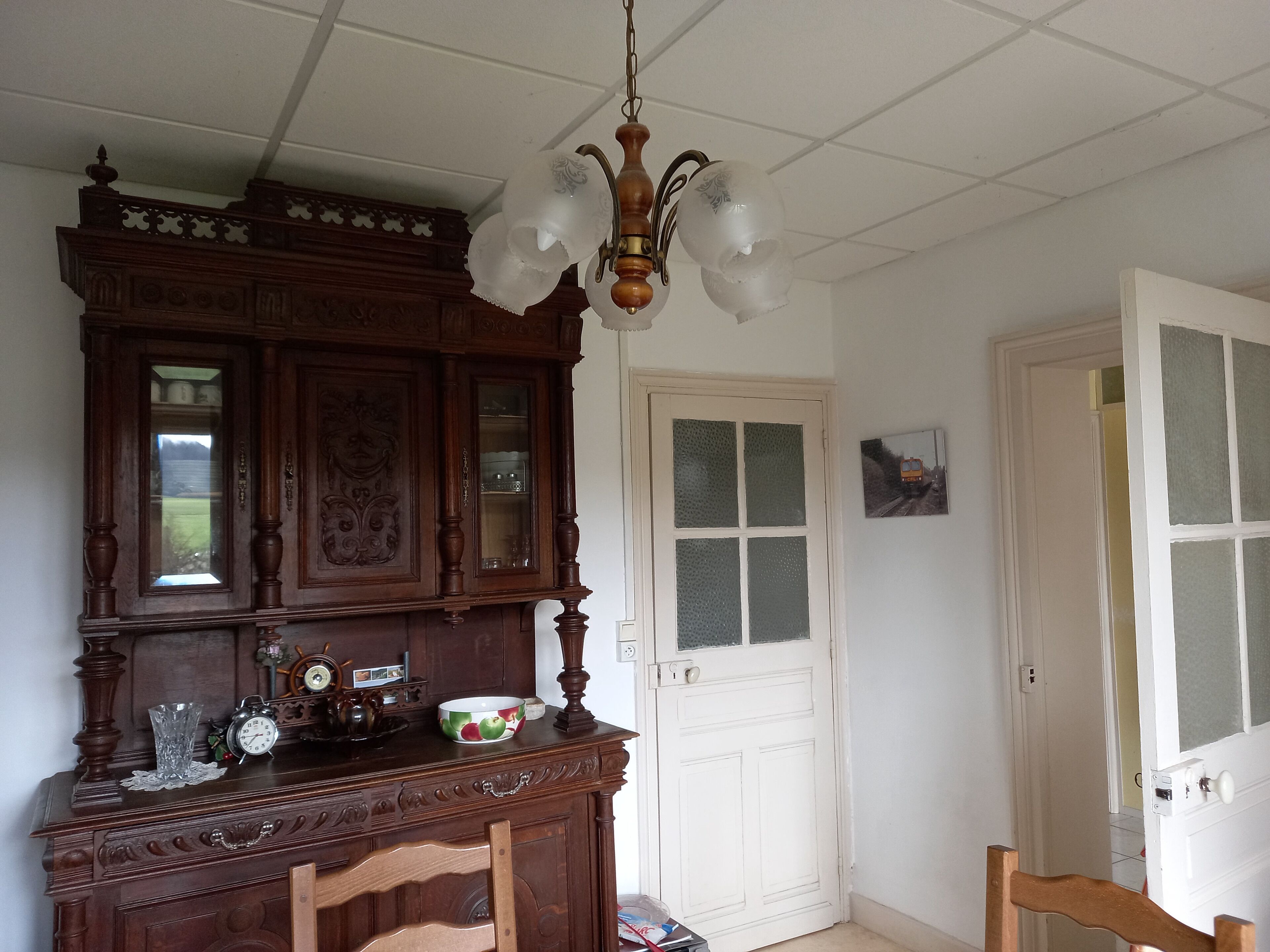 Une pièce avec un meuble en bois, une porte blanche et un luminaire suspendu.