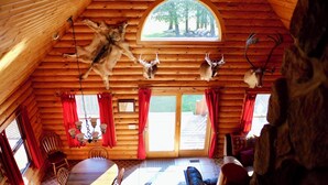 A log cabin interior with a dining area, a fireplace, and mounted animal heads on the ceiling.